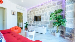 A modern living room with a stone wall, a flat-screen TV, a red sofa, a white console table, and a potted plant. - Apartments None & Nono-Comfort One-Bedroom Apartment with Shared Terrace (Cavtat)