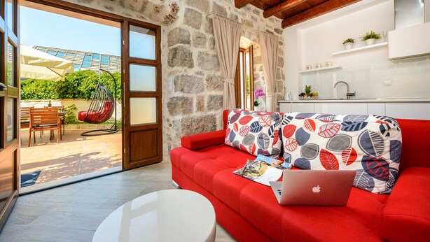 A modern living room with a red sofa, a laptop, and a dining area with a table and chairs. - Apartments None & Nono-Comfort One-Bedroom Apartment with Shared Terrace (Cavtat)