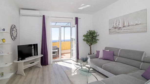 A modern living room with a flat-screen TV, grey sofa, and a glass coffee table.
