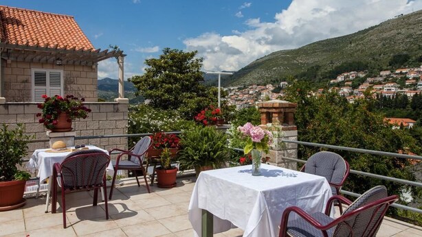Une terrasse avec une table et des chaises, des plantes en pot et une vue sur la ville et les collines.