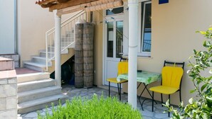 Un espacio al aire libre techado con una escalera que lleva a una puerta, dos sillas amarillas y una mesa con mantel verde.