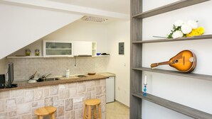 Una cocina con encimera de piedra, taburetes de madera, lavavajillas integrado y un estante en la pared con una guitarra y flores.