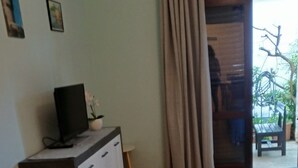 A bedroom with a wooden floor, a sofa, a bed, a TV on a dresser, and a view of the outdoors through a door. - Apartments Magda- Comfort Studio Apartment with Patio (Cavtat)