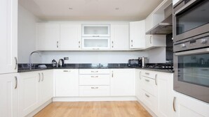 A modern kitchen with white cabinets, a black countertop, and stainless steel appliances including a double oven. - Penthouse B (Newquay)