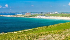 A coastal view with a beach, a grassy area, and buildings in the background. - Penthouse B (Newquay)
