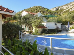 A pool area with a stone pathway, a white building with a red roof, and a mountainous backdrop. - Villa Klara - Holiday Home with Terrace, Pool and Sea View (Viganj)