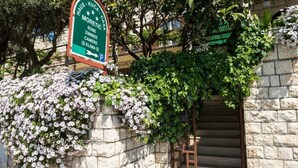 Un mur de pierre sur lequel est apposée une plaque indiquant une maison nommée « Haus - Kuca Casa », et un escalier menant à une porte.