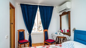 Un dormitorio con cama, dos sillas, una mesa con espejo y una ventana con cortinas.