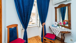 Una habitación con piso de madera, una mesa con mantel de encaje, una silla con cojín rojo y un espejo en la pared.