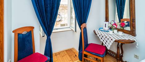 A room with a wooden floor, a table with a lace tablecloth, a chair with a red cushion, and a mirror on the wall.