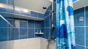 Un baño con azulejos azules y blancos, una ducha con cabezal de ducha manual y un estante con artículos de aseo.