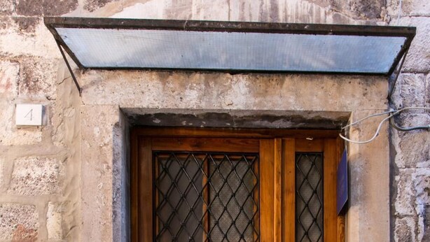 Una puerta de madera con una reja metálica, ubicada en un edificio de piedra con unos pocos escalones de piedra que conducen a ella.