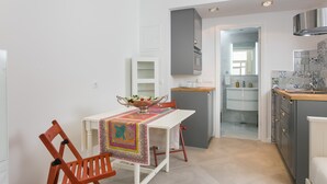 Eine kompakte Küche mit weißen Schränken, einer Holz Arbeitsplatte und einem Essbereich mit Tisch und Stühlen.