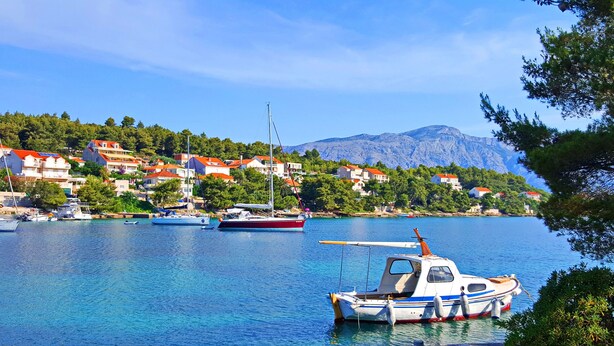 Un village côtier où des bateaux sont amarrés le long de la rive, entouré de maisons aux toits rouges et dominé par un paysage montagneux.