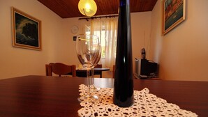 Une table à manger recouverte d’une nappe en dentelle, un verre à vin et une bouteille de vin. Des chaises sont disposées autour de la table, et un tableau est accroché au mur.