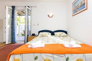 A hotel room with an open door leading to a balcony, a bed with an orange blanket, and a painting on the wall.