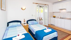 Een kamer met twee bedden, een klein nachtkastje met lamp, een deur naar een balkon en een kitchenette met een spoelbak en fornuis.