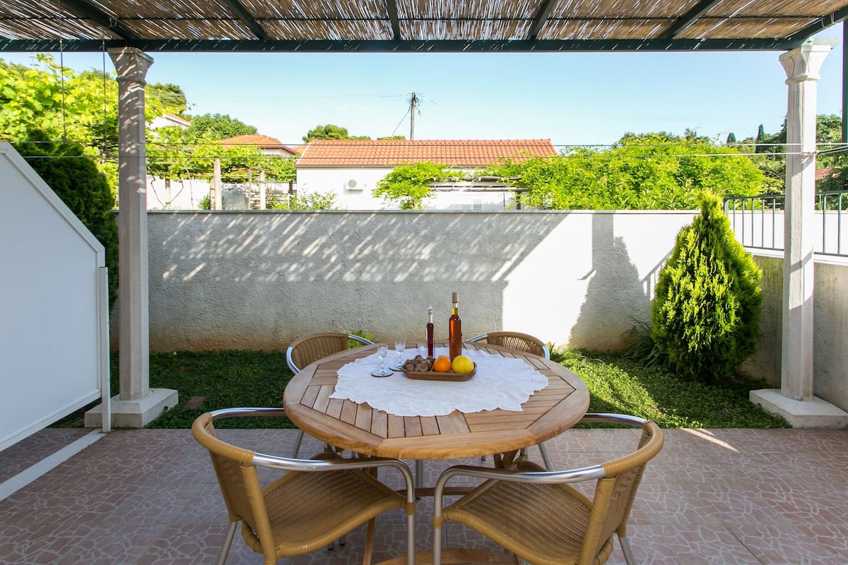 A covered patio with a round wooden table set for four, surrounded by wicker chairs.