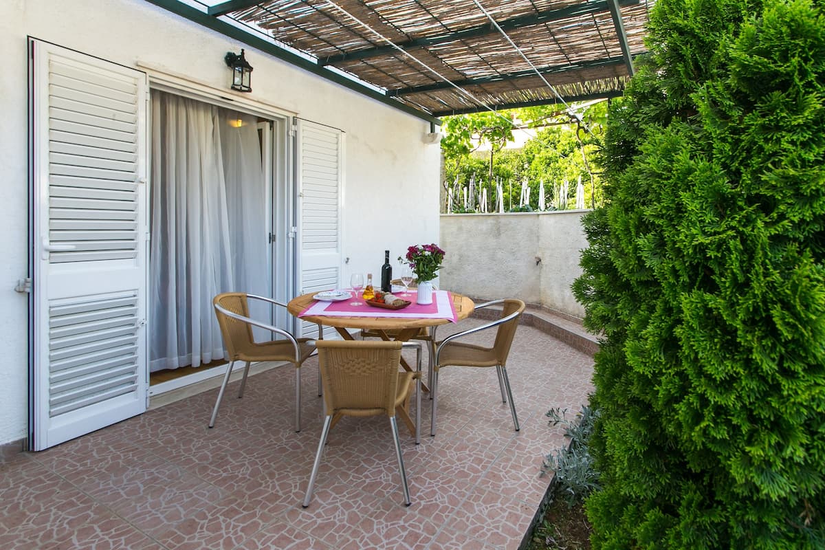 An outdoor patio with a round table and four chairs, a bottle of wine, and a vase of flowers.
