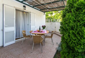 An outdoor patio with a round table and four chairs, a bottle of wine, and a vase of flowers.
