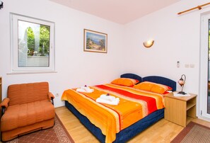 Une chambre à coucher comprenant un lit, une chaise, une table de chevet, une lampe, un tableau et une fenêtre.