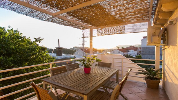 Ein Holztisch mit Stühlen auf einem Balkon, mit Blick auf Häuser und einen Strommasten.