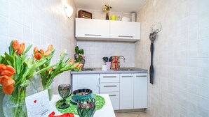 Ett kök med vita skåp, en bänkskiva och ett stänkskydd. På bänkskivan står vaser med blommor, en skål och ett vinglas.