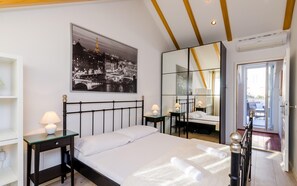Un dormitorio moderno con cama, mesitas de noche, un espejo y un cuadro con vista a la ciudad.