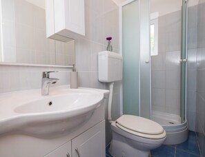 Un baño con lavamanos blanco, inodoro y cabina de ducha con mampara de vidrio.