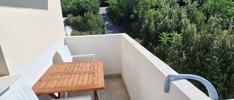 A balcony with a wooden table and two white chairs, overlooking a forested hillside.