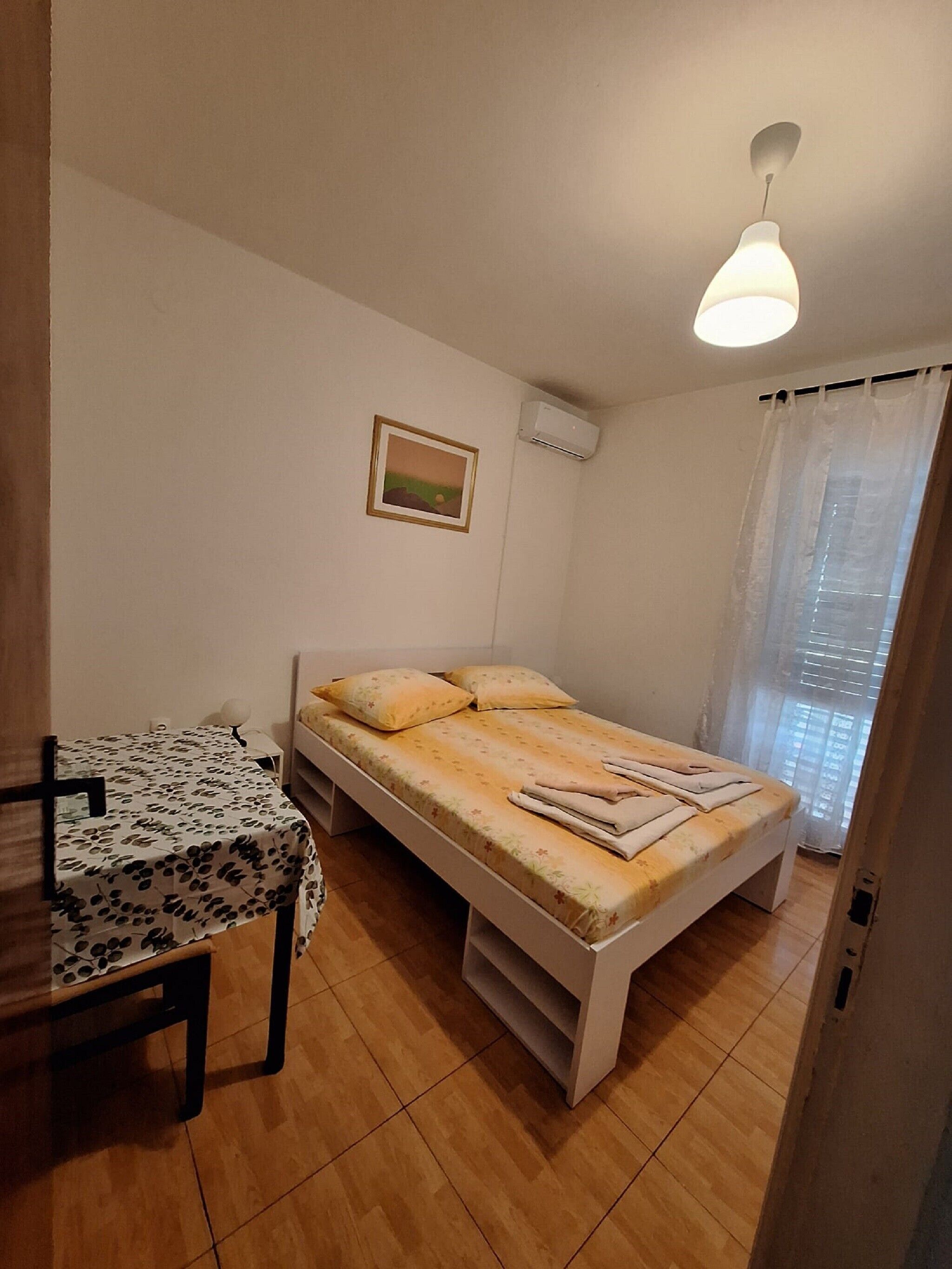 Una habitación pequeña y limpia con una cama individual, una mesa y un cuadro en la pared.