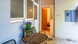 En terrasse med et træbord og stole, et velkommenskilt, en potteplante og et skilt der viser vejen til kontoret for lejlighedsadministrationen.