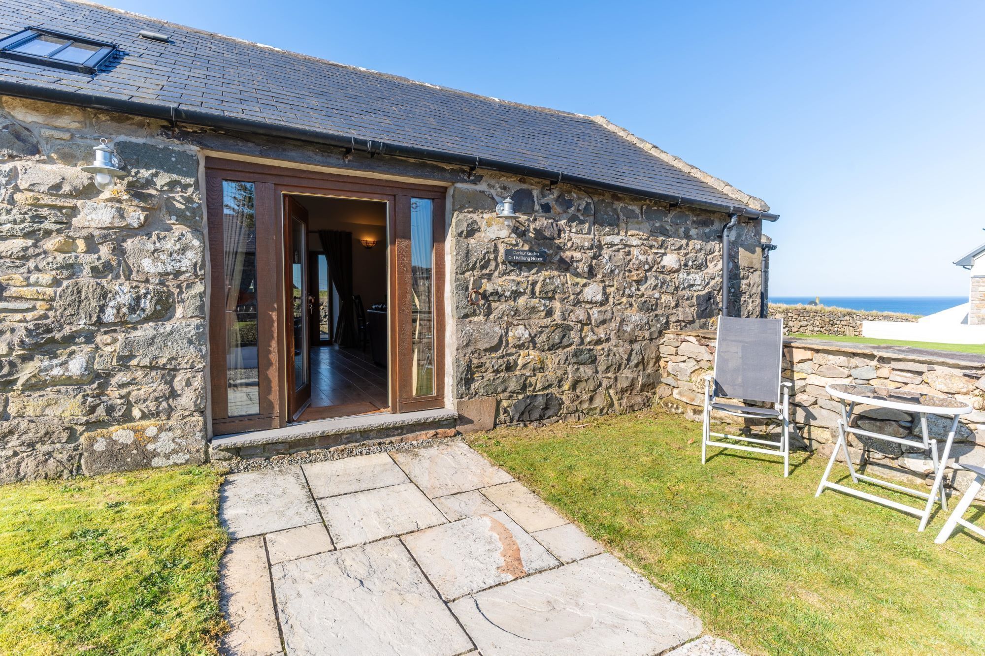 A stone building with a wooden door, a small porch, and a view of the sea.