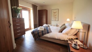 A bedroom with a bed, bedside table, lamp, and a view of the outside. - The Tack Room (Pwllheli)