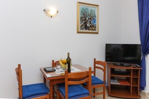 A dining area with a table, chairs, a painting, a television, and a bottle of wine.
