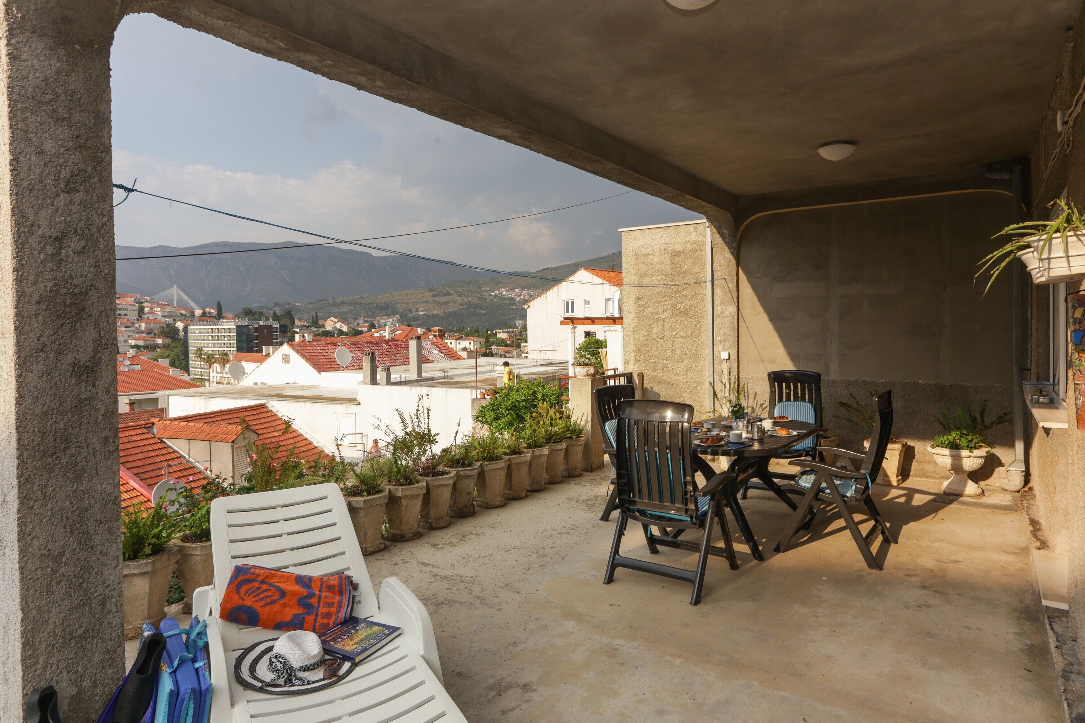 A balcony with a table and chairs, potted plants, and a view of the cityscape.