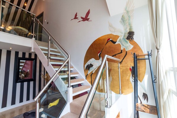 Una escalera con barandales de vidrio y un mural en la pared con aves.