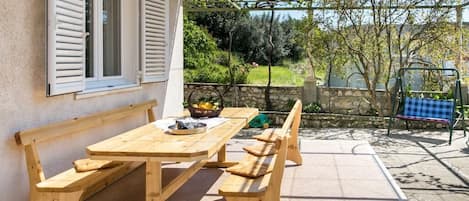 An outdoor wooden table and benches with a stone wall and greenery in the background.