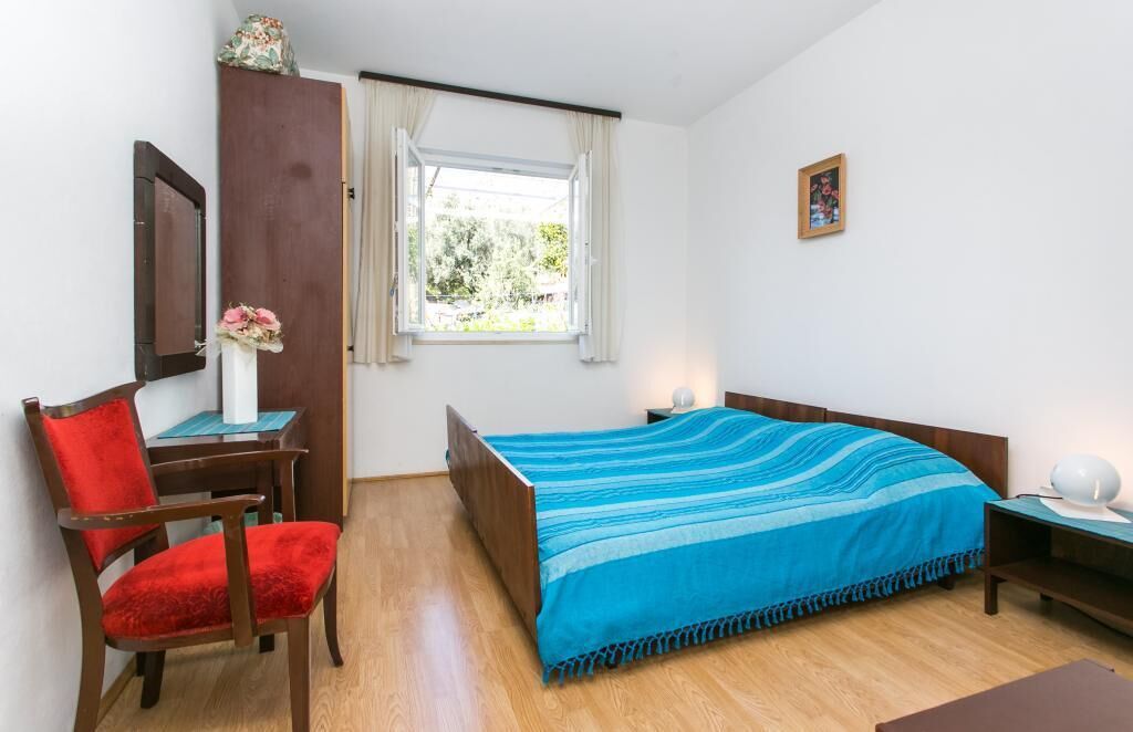 A bedroom with a bed, a chair, a desk, a window, and a picture on the wall.