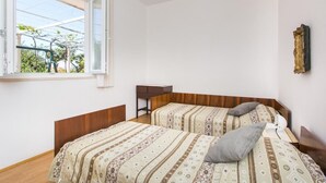 A bedroom with two beds, a window with a view of greenery, and a small table. - Apartment Marko - Three-Bedroom Apartment with Terrace and Sea View (Brsečine) (Brsecine)