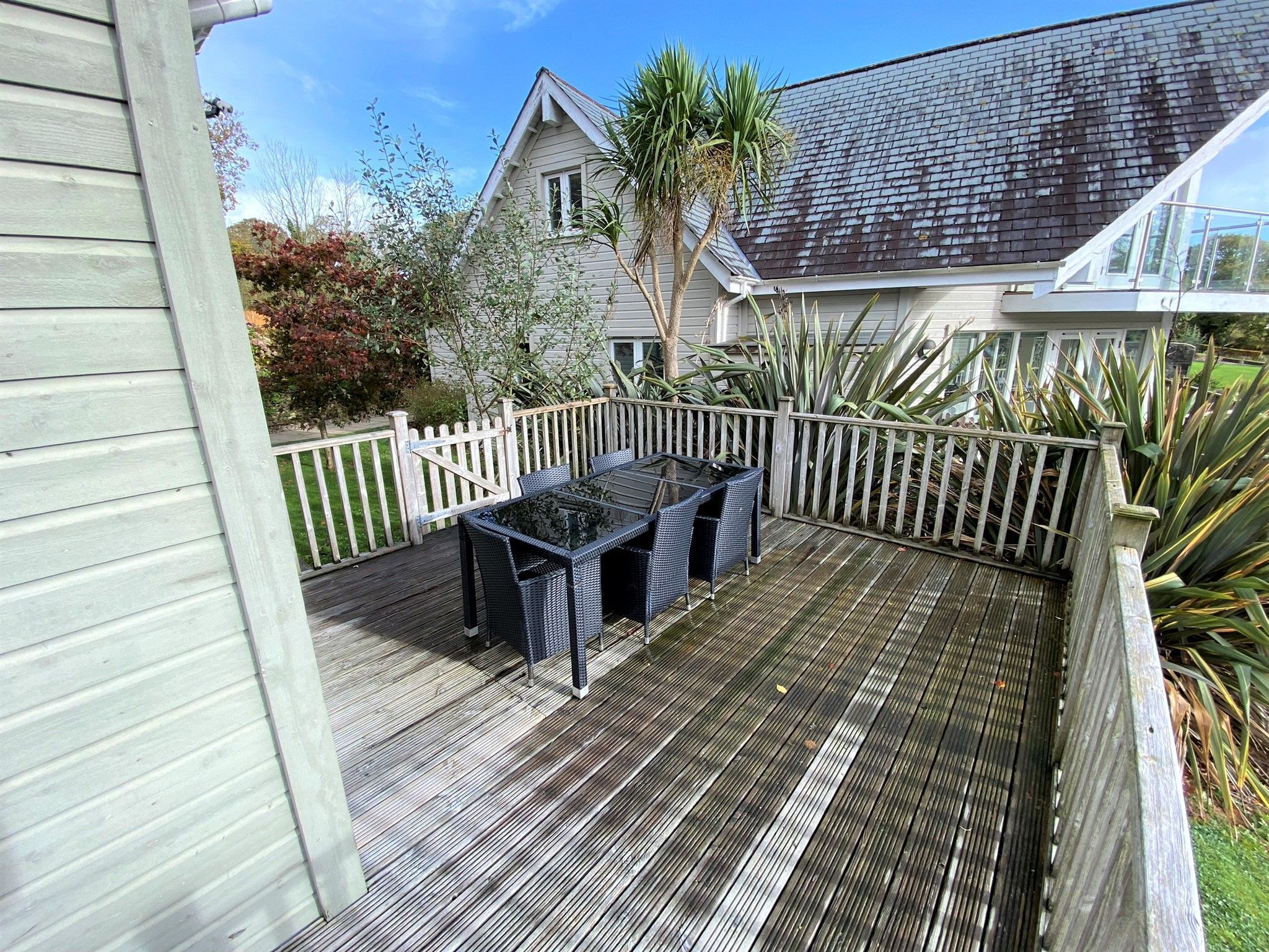 A wooden deck with a glass-top table and chairs, surrounded by a white picket fence.