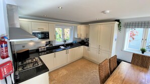 Une cuisine moderne avec des meubles blancs, un plan de travail noir, une cuisinière à gaz et un coin repas comprenant une table en bois et des chaises en osier.