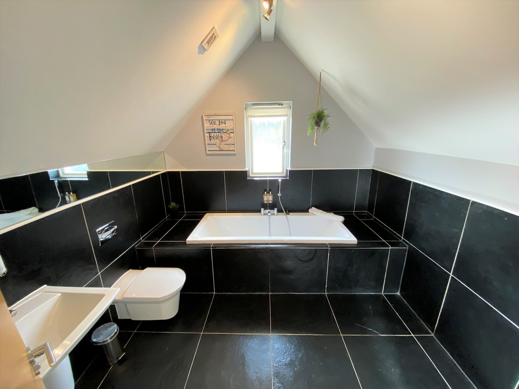 A modern bathroom with a black and white tiled floor, a white bathtub, a white sink, and a toilet.