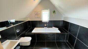 A modern bathroom with a black and white tiled floor, a white bathtub, a white sink, and a toilet.