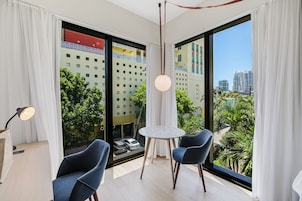 Una habitación moderna con un ventanal grande, dos sillas, una mesita redonda y una lámpara colgante.