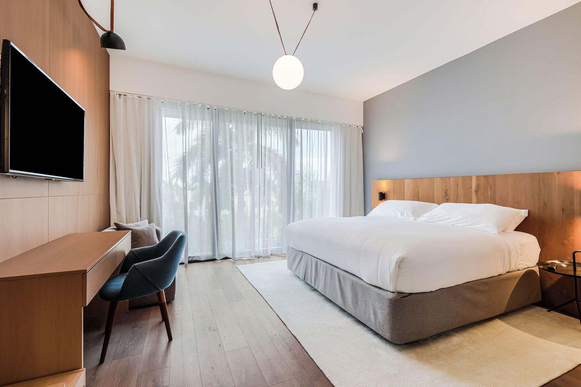 A modern hotel room with a large bed, a desk, a chair, and a TV.