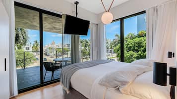 Un dormitorio con una cama grande, vistas de la ciudad a través de un ventanal corredero y un balcón con mesa y sillas.