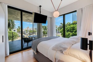 Un dormitorio con una cama grande, vistas de la ciudad a través de un ventanal corredero y un balcón con mesa y sillas.