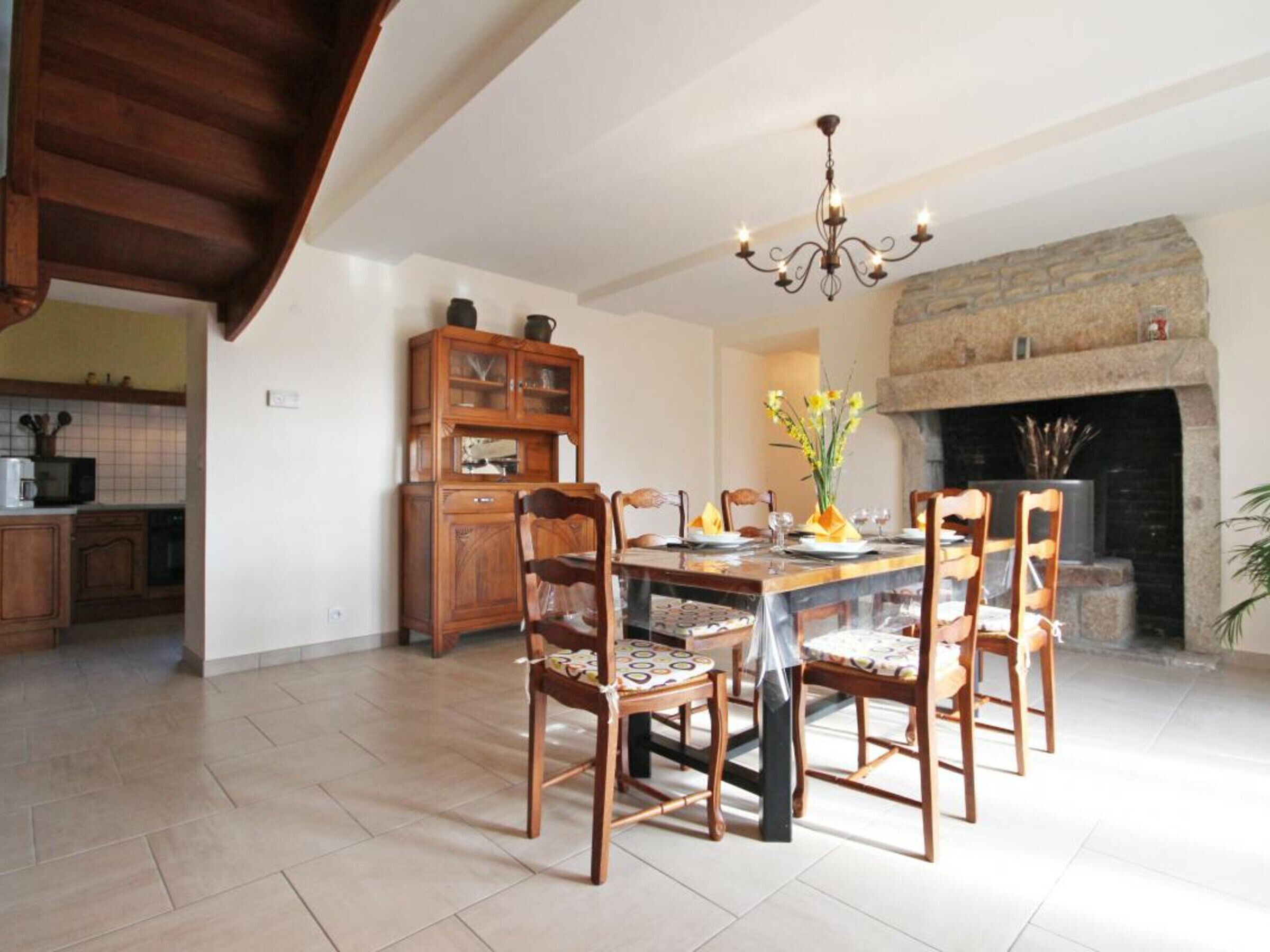 A dining area with a wooden table and chairs, a chandelier, and a stone fireplace.