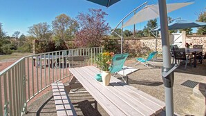 Une terrasse extérieure avec une table en bois, des chaises et des parasols pour créer de l’ombre.